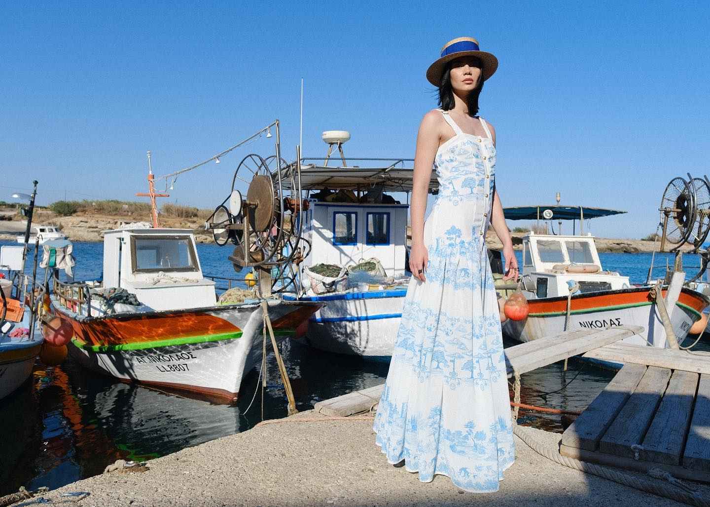 Woman in a floral dress standing on a dock with boats in the background