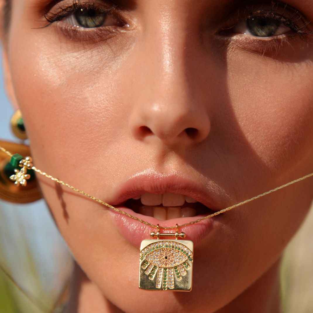 Close-up of a woman wearing a gold necklace with an eye-shaped pendant.