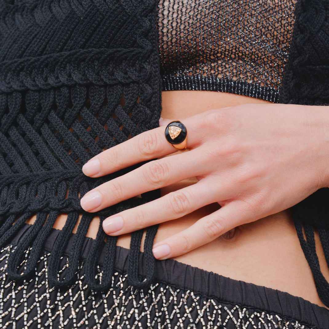 Close-up of a hand wearing a black ring with a gold triangle on a black textured garment.