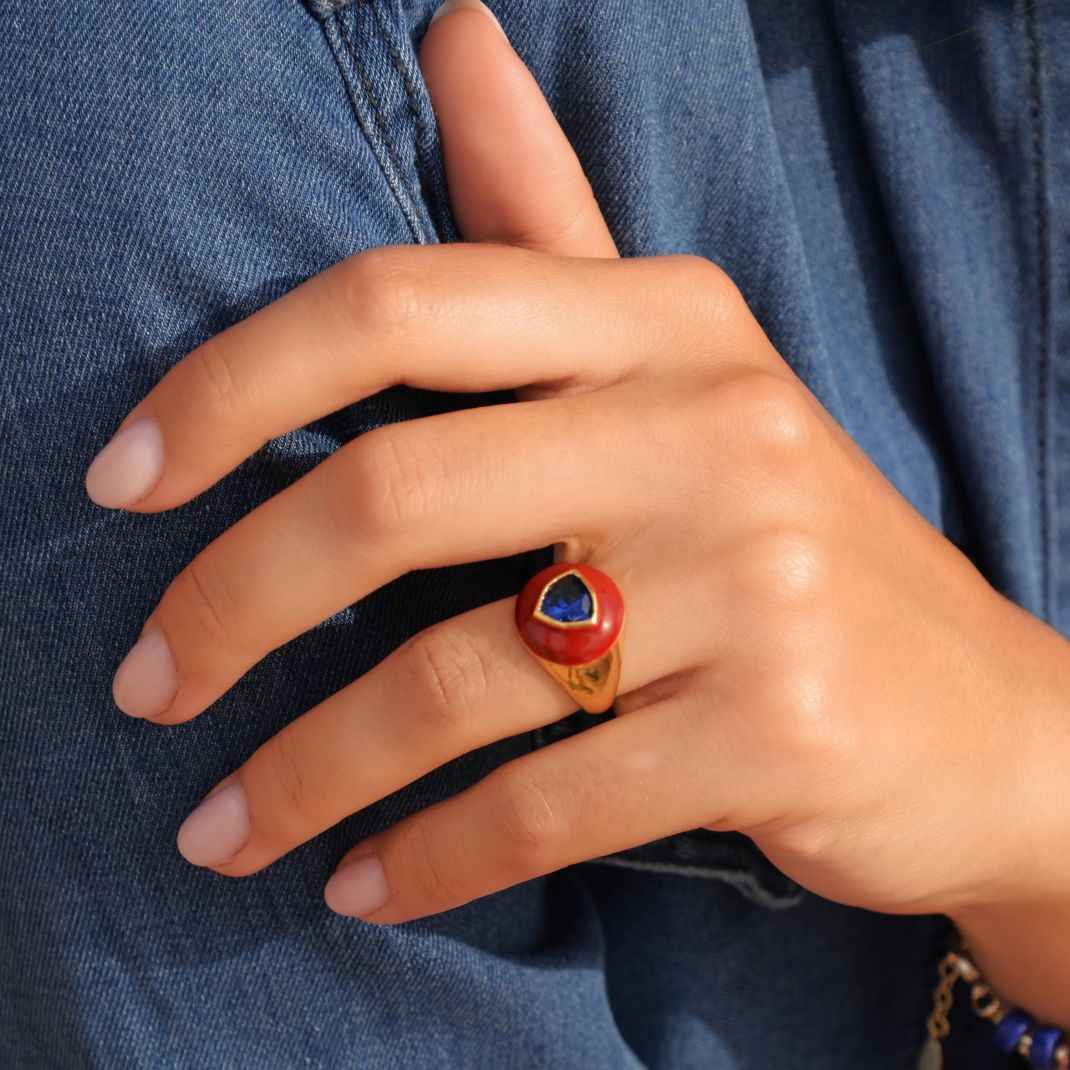 Hand wearing a ring with a red stone against a denim background