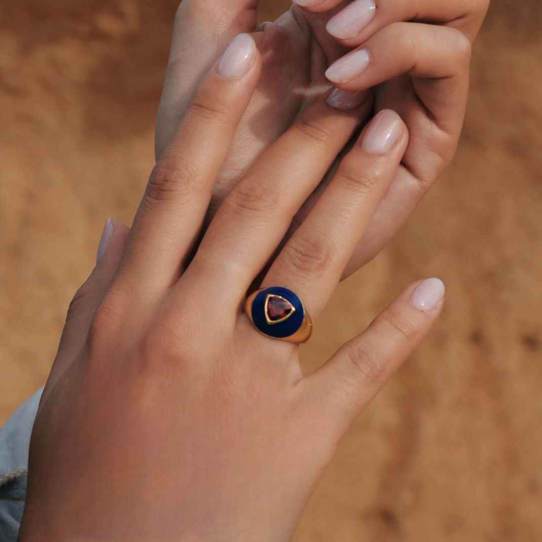 Hand wearing a ring with a heart-shaped gemstone against a blurred background