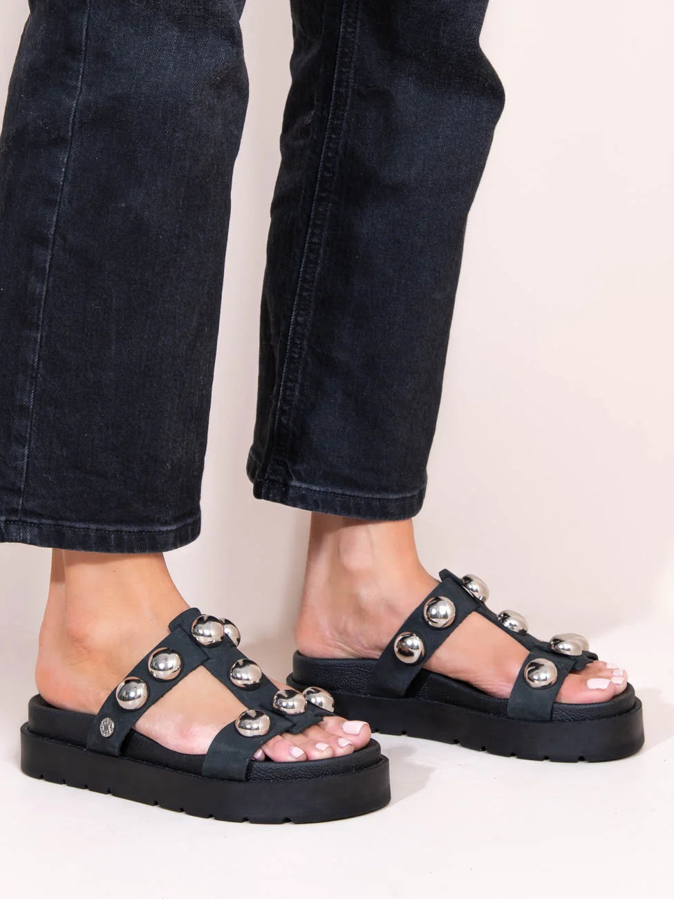 Black sandals with silver embellishments worn with black jeans on a light background