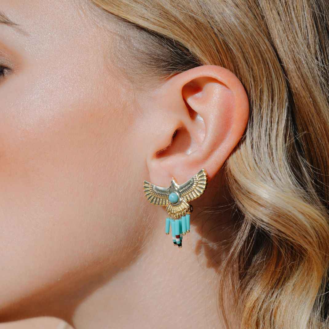 Close-up of an ear wearing a gold and turquoise earring with blonde hair.