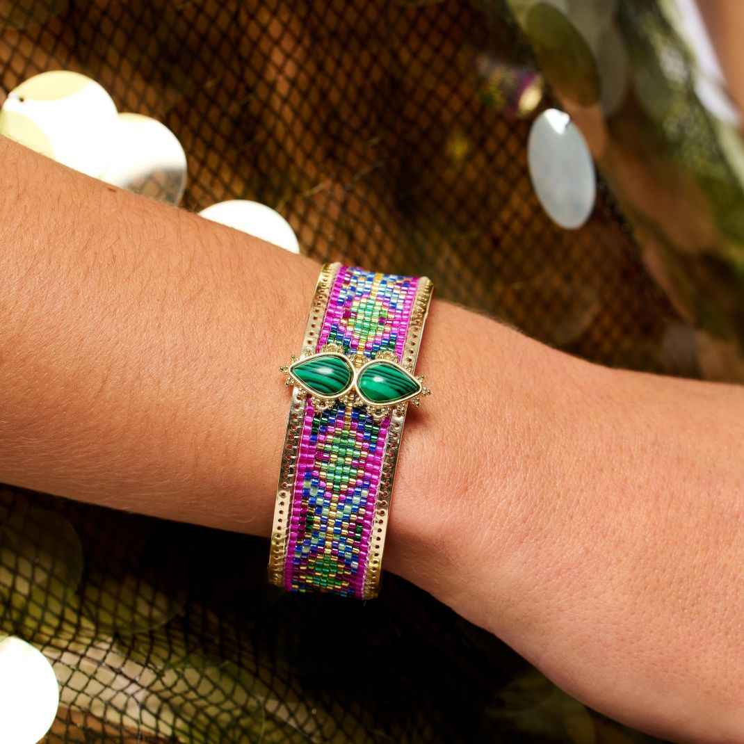 Multicolored beaded bracelet with green gemstones on a wrist against a patterned background