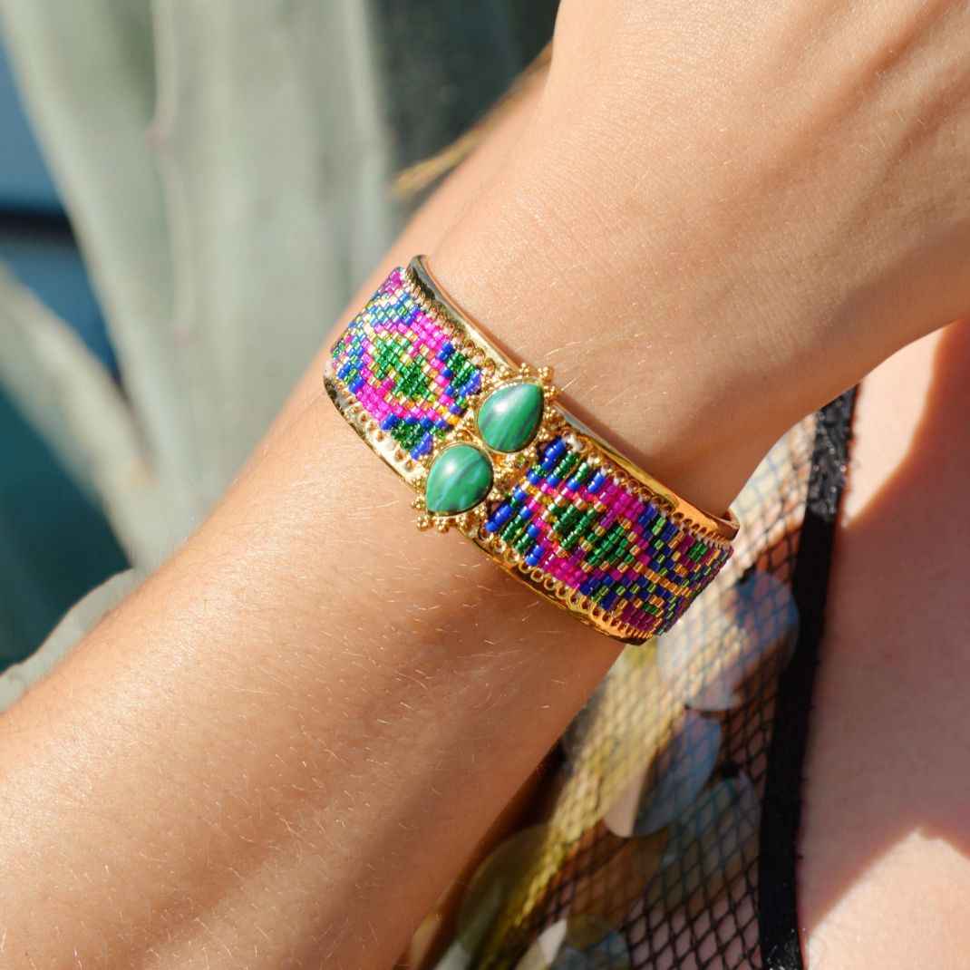 Multicolored beaded bracelet with green stones on a wrist against a blurred background