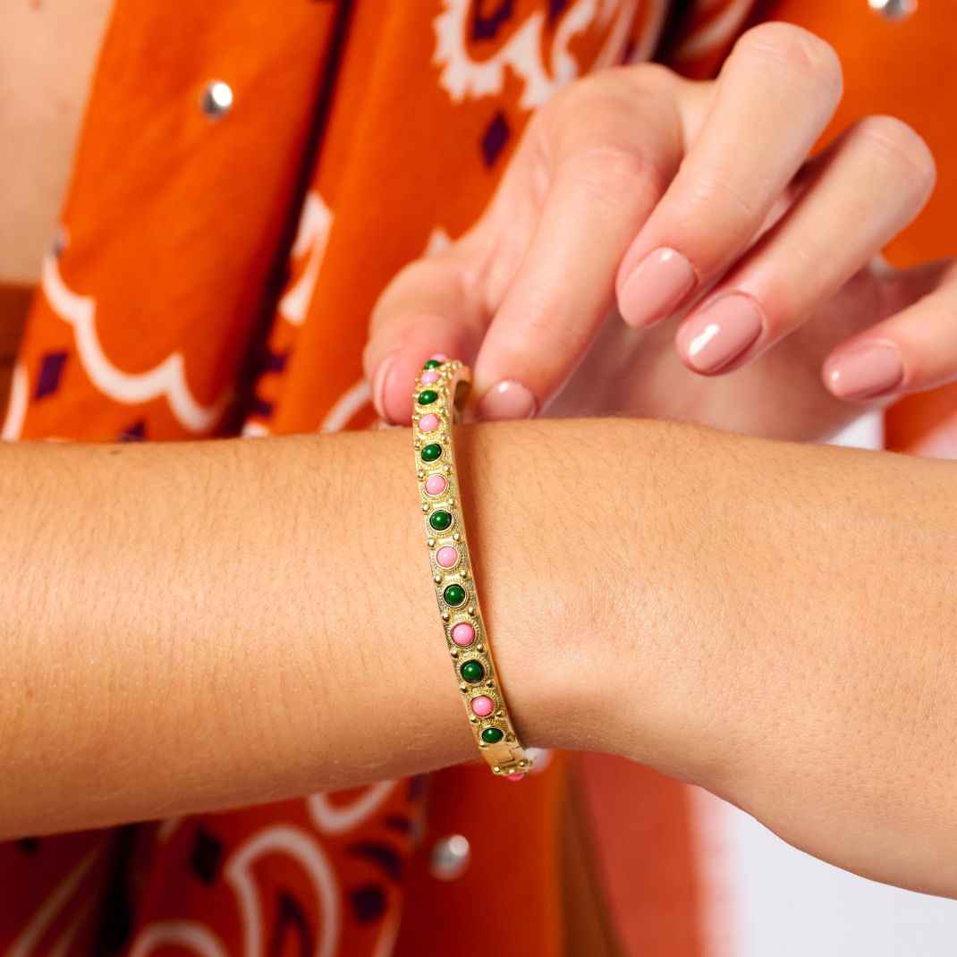 Gold bracelet with colorful stones on a wrist against an orange patterned background
