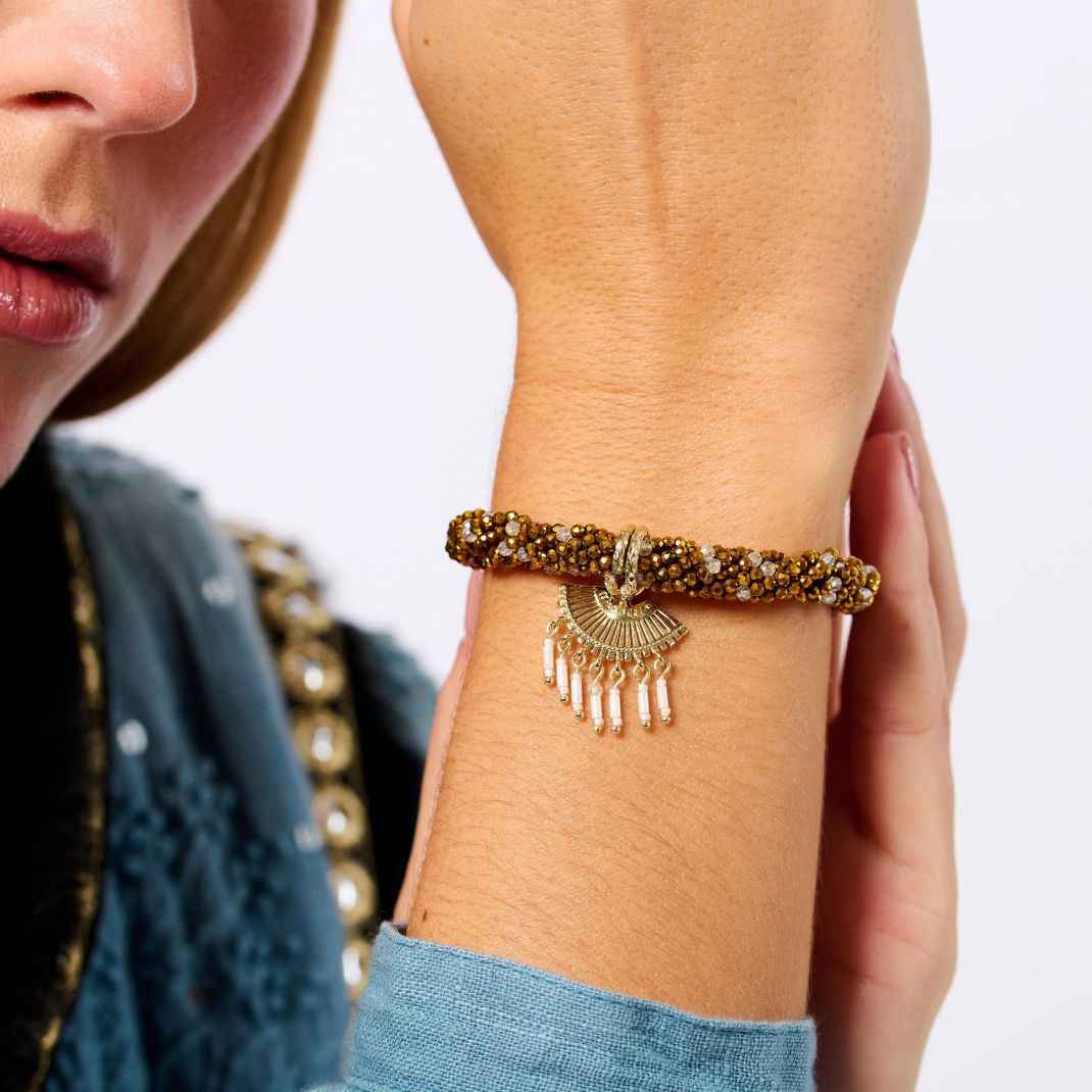 Close-up of a person wearing a gold bracelet with a decorative clasp on a plain background
