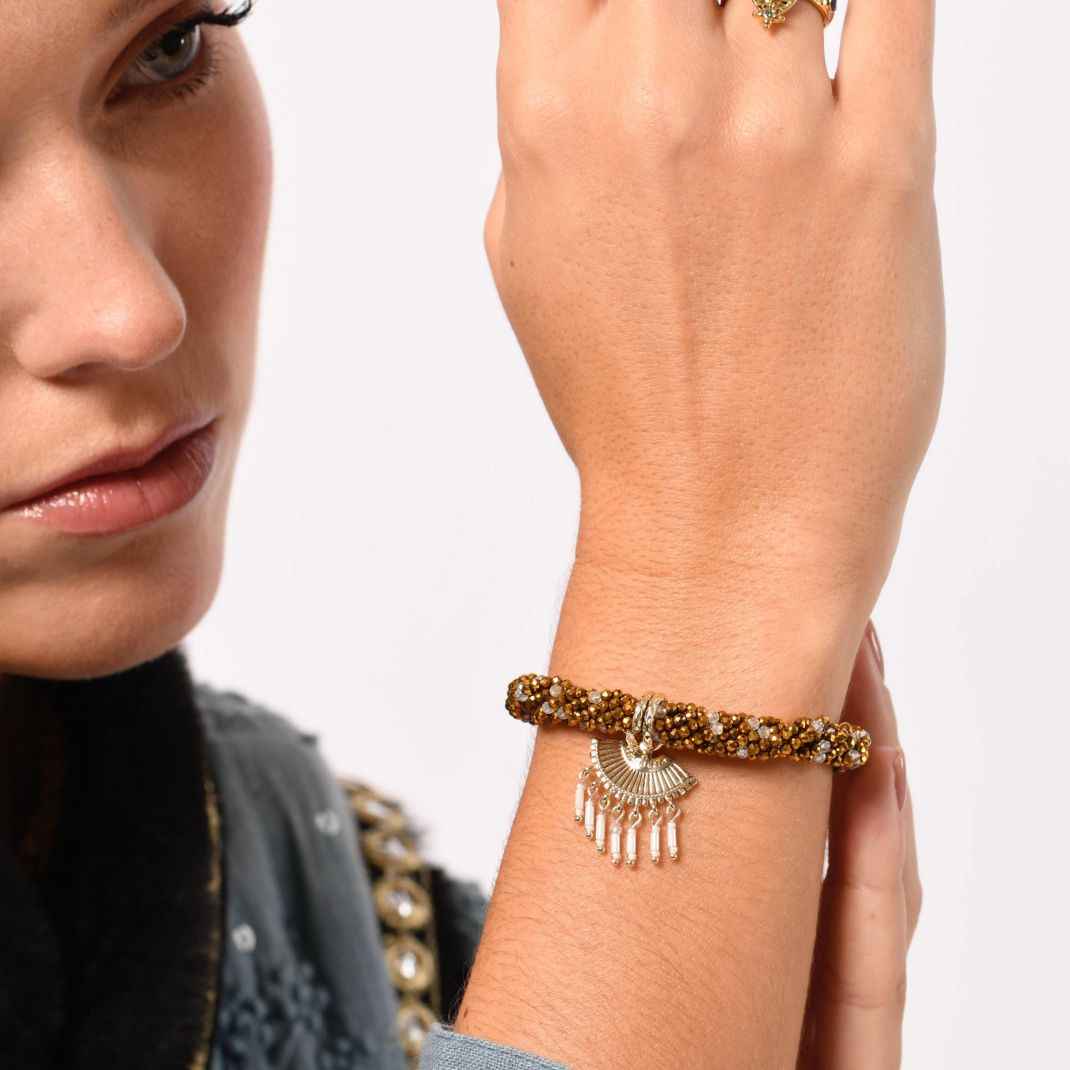 Close-up of a woman's wrist wearing a gold bracelet with a neutral background