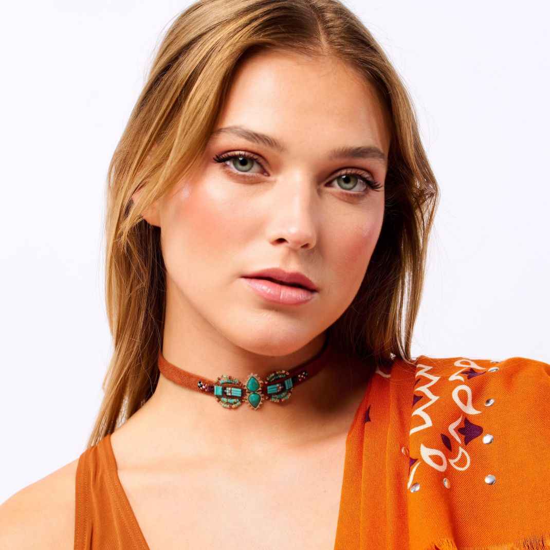 Woman wearing an orange top and turquoise choker necklace on a white background
