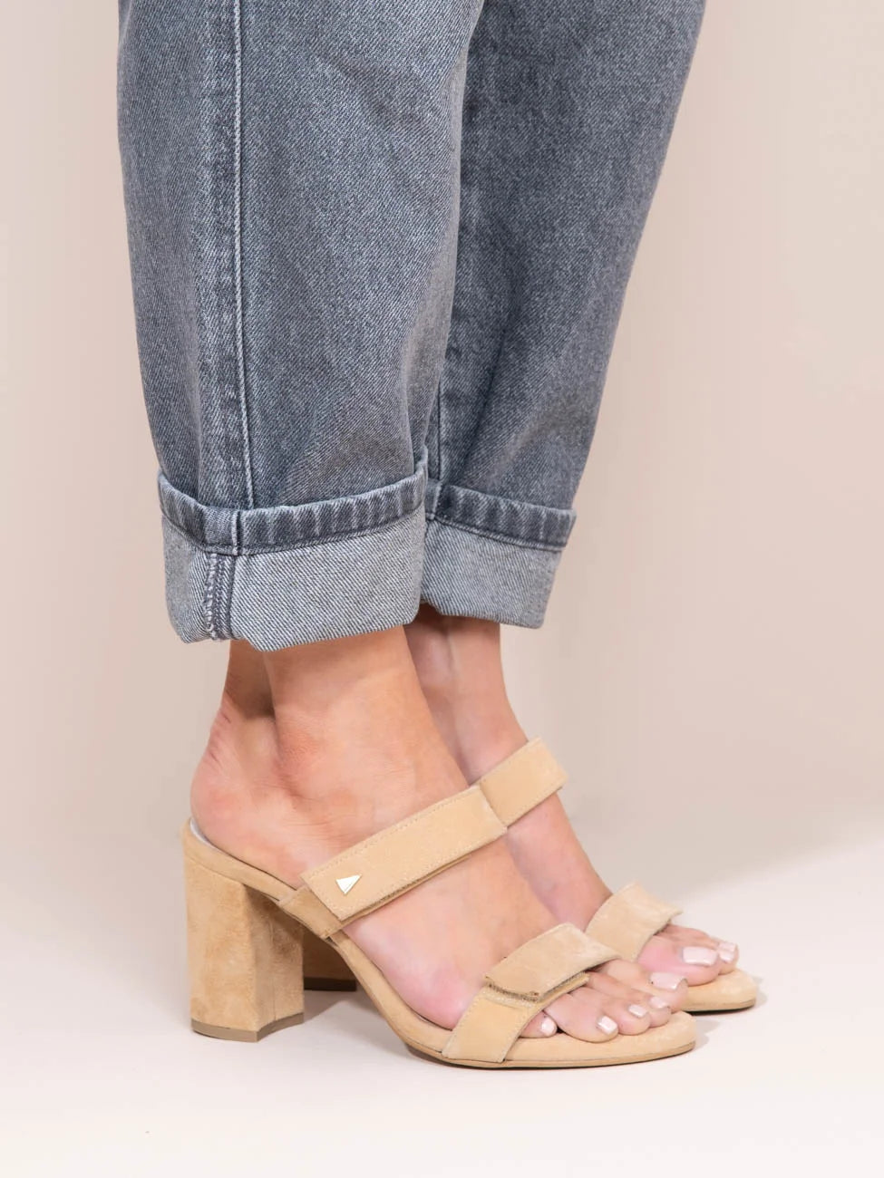 Beige sandals worn with rolled-up jeans on a neutral background