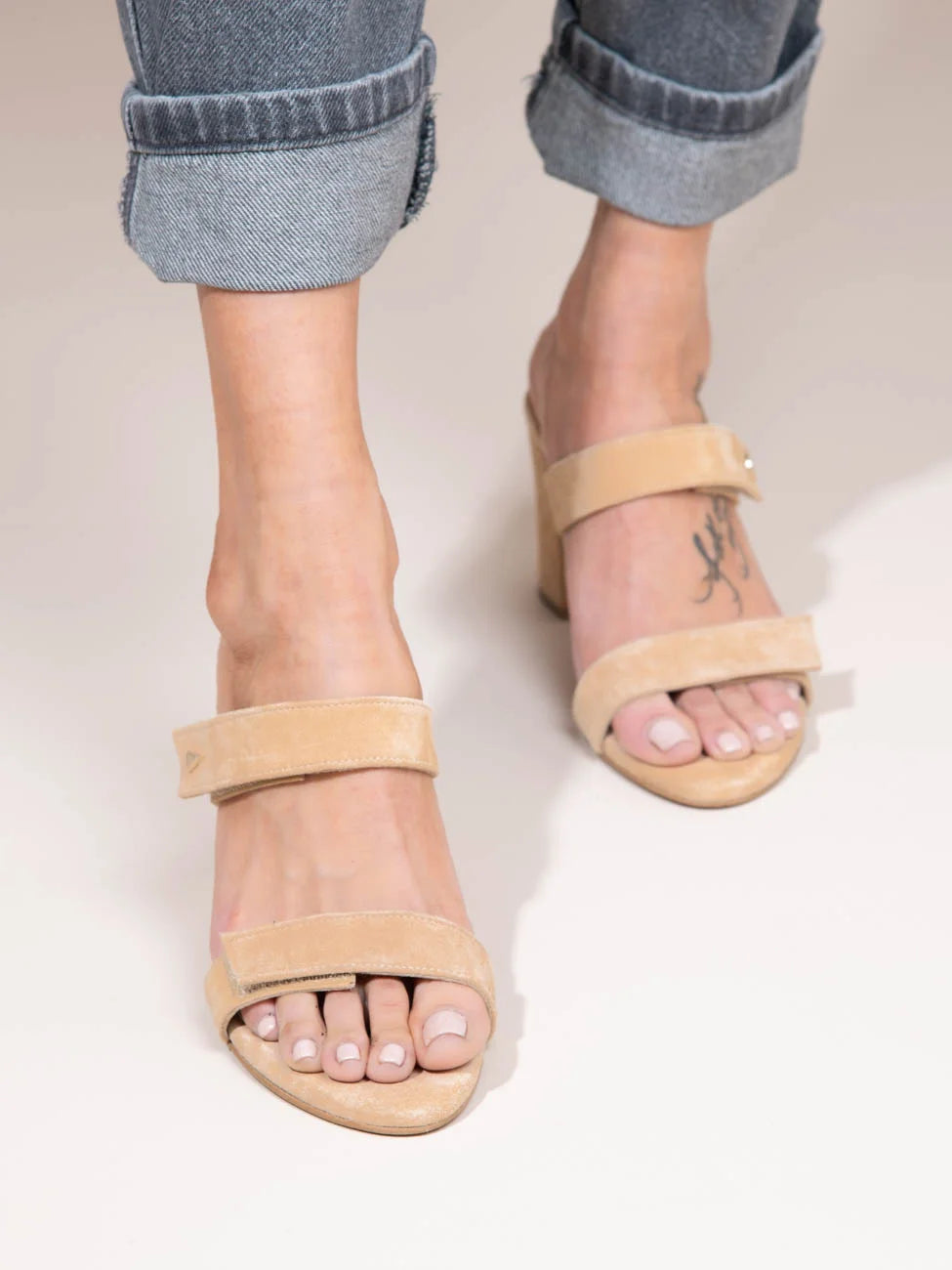Beige sandals worn with rolled-up jeans on a light background