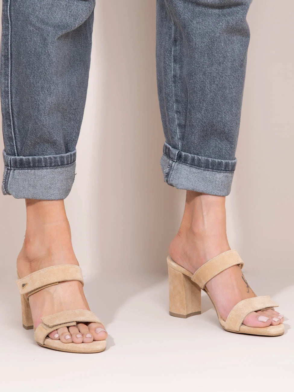 Beige sandals worn with rolled-up jeans on a neutral background
