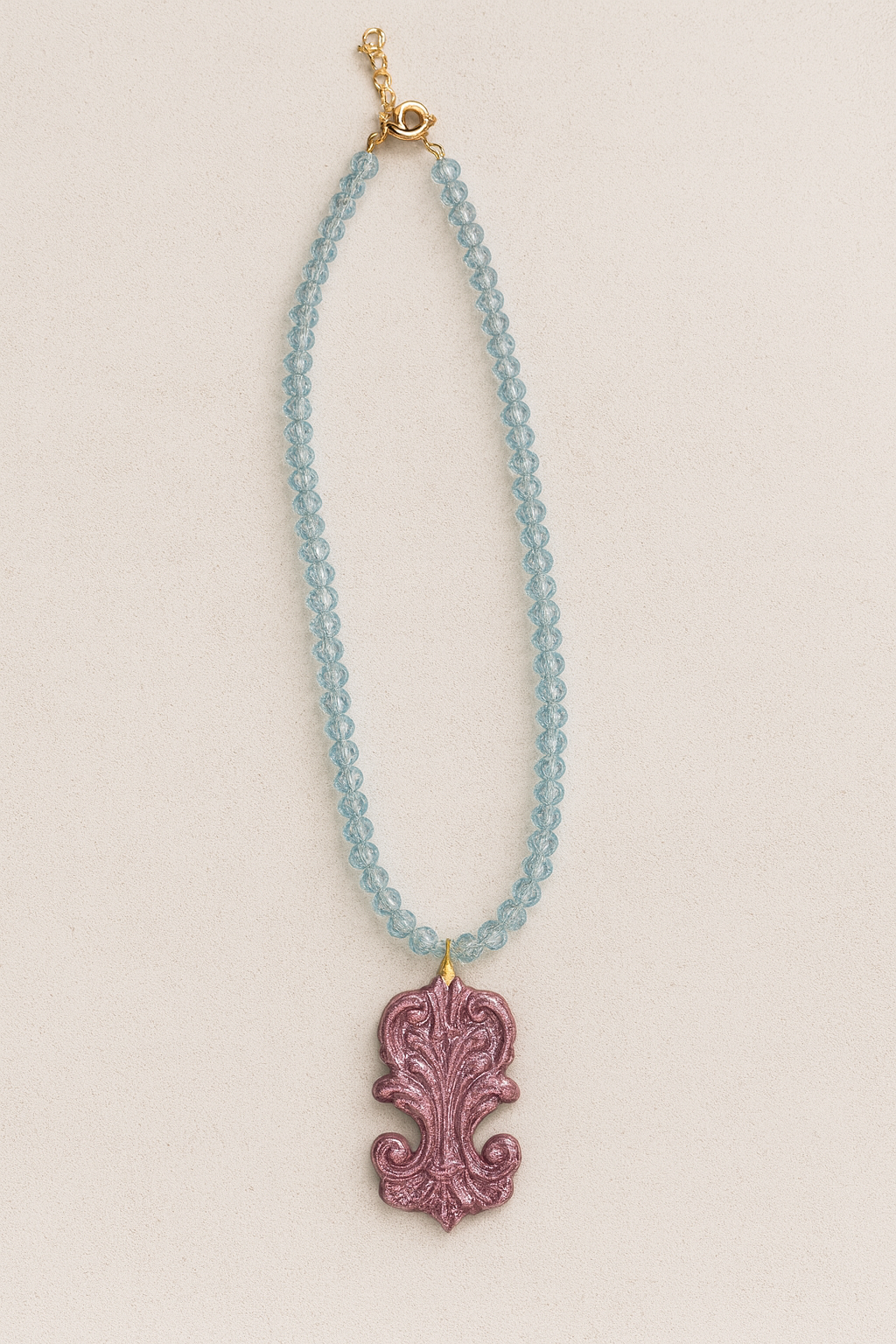 Necklace with blue beads and a pink decorative pendant on a beige background