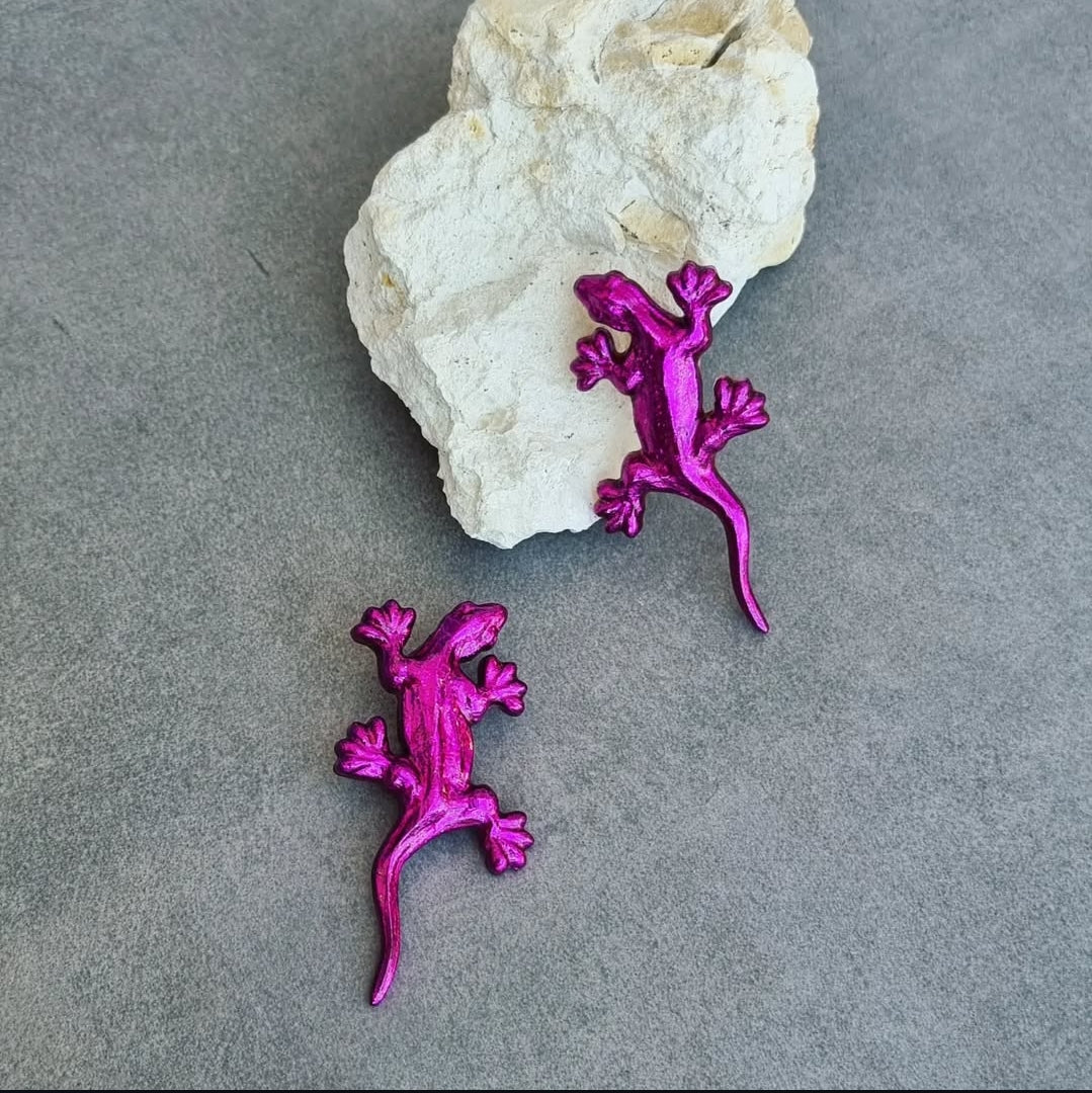 Two pink gecko-shaped objects on a gray surface with a rock in the background.