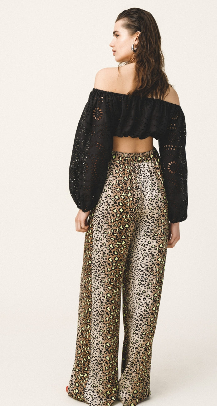 Woman wearing a black off-shoulder top and leopard print pants on a white background