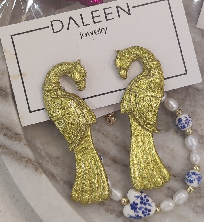 Gold fish-shaped earrings on a Daleen jewelry card with a marble surface.