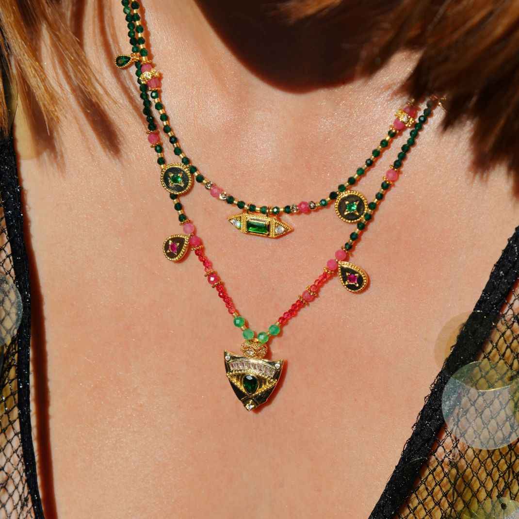 Necklace with green and red beads and gold pendants on a person wearing a black mesh top.