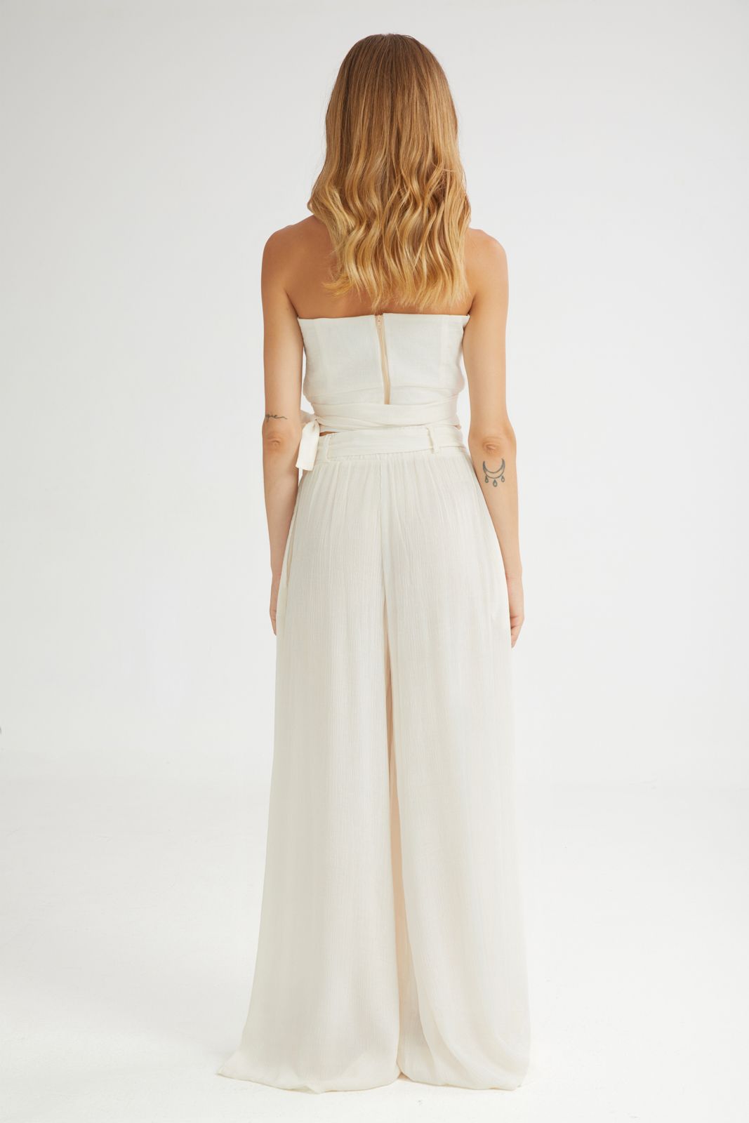 Woman wearing a strapless white jumpsuit on a plain background