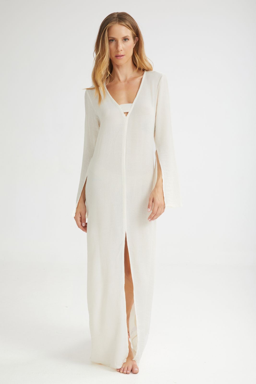 Woman wearing a long, light-colored dress with a slit on a white background