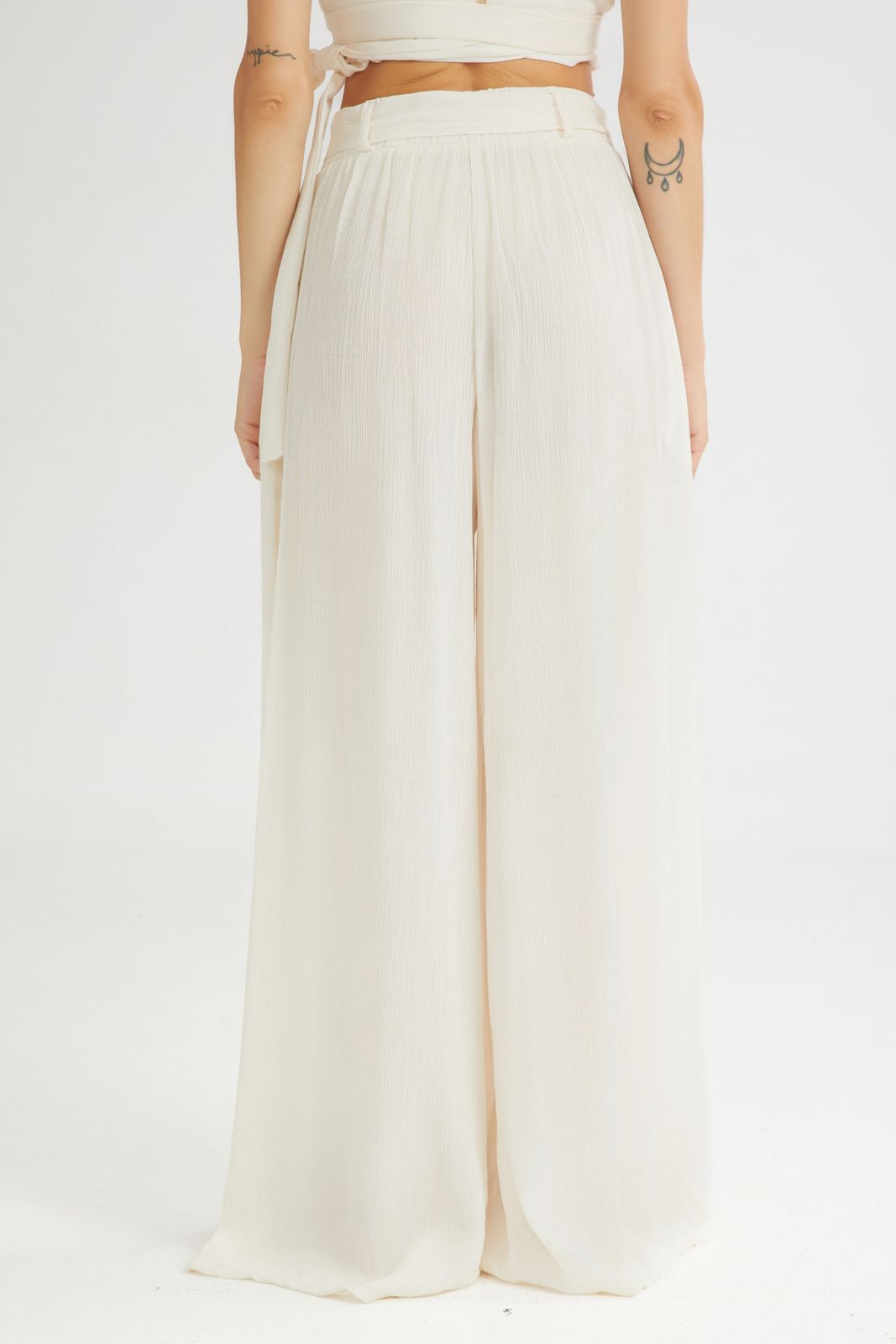 Person wearing a white outfit with wide-leg pants on a plain background