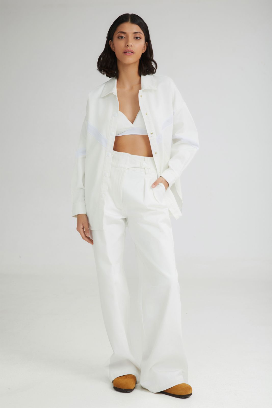 Woman wearing a white outfit with a jacket and pants on a plain background