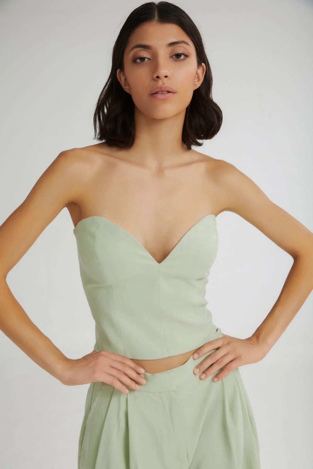 Woman wearing a light green strapless top and skirt set against a plain background