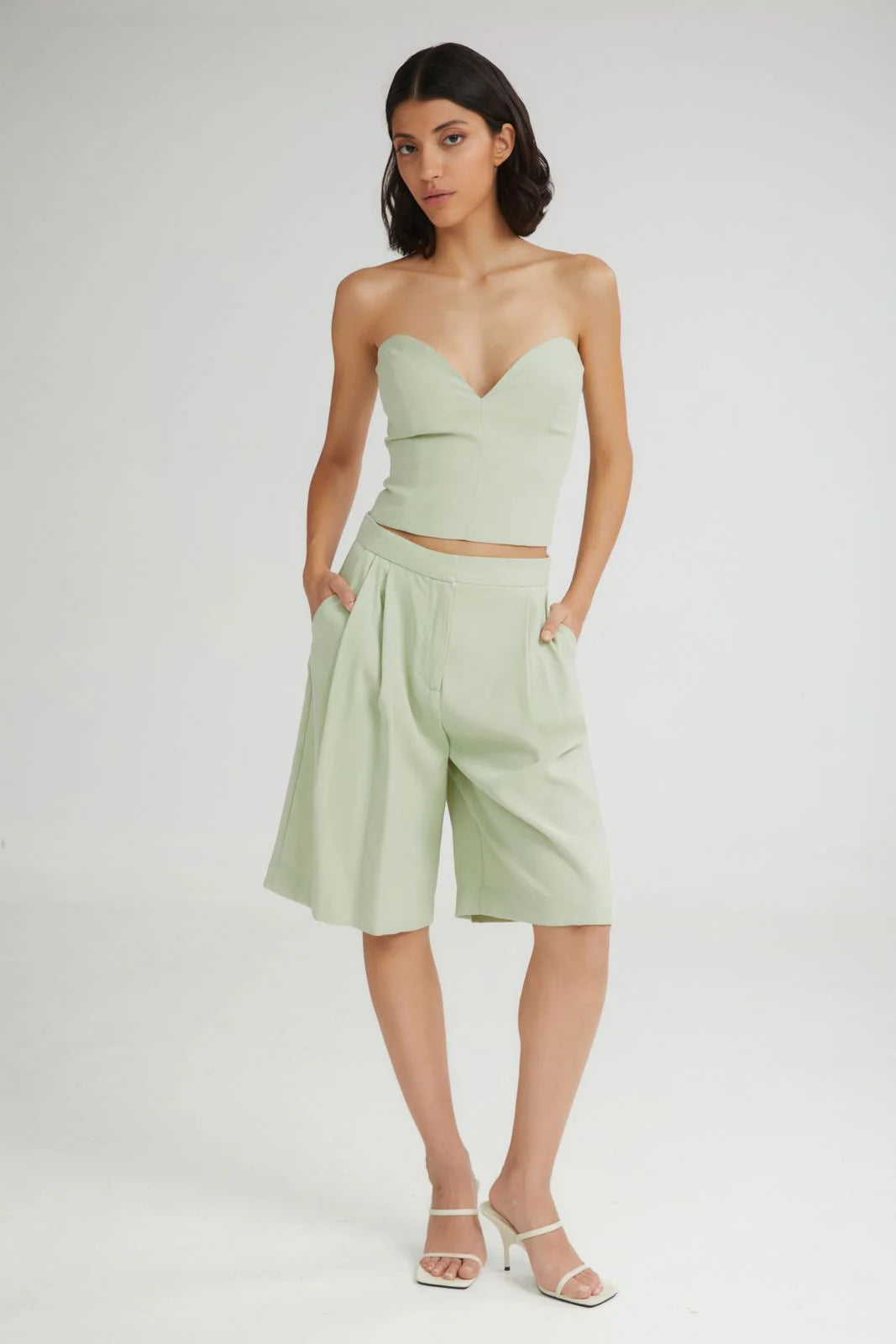 Woman wearing a light green strapless top and high-waisted shorts on a white background