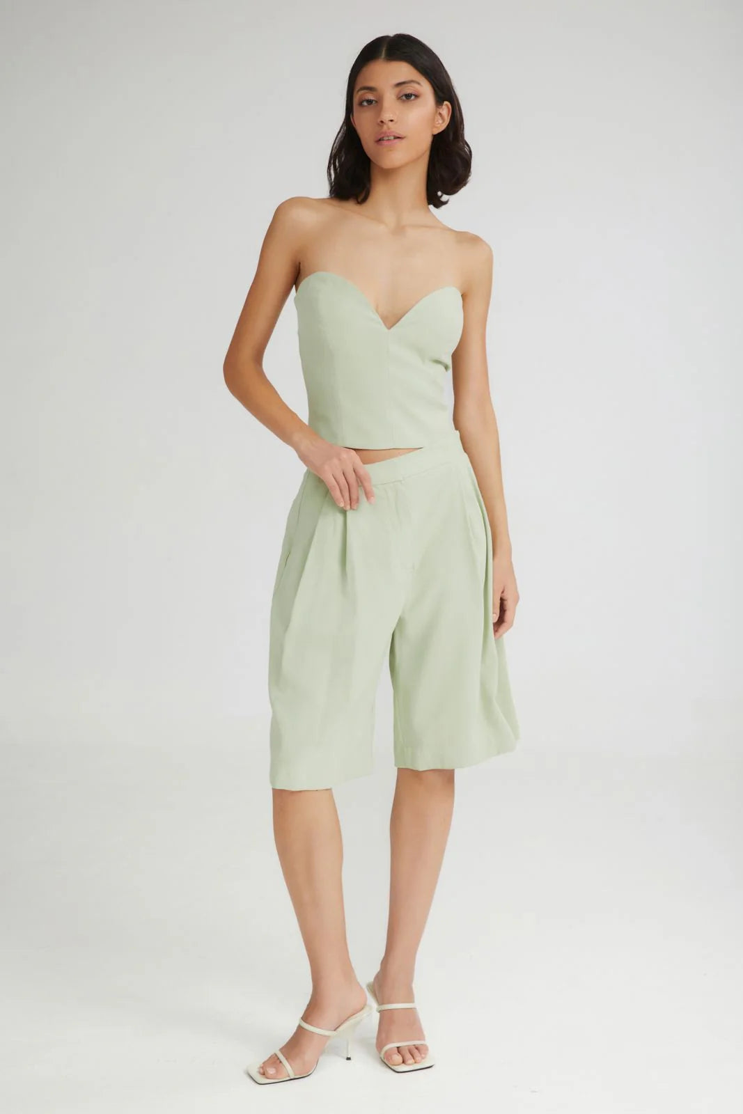 Woman wearing a light green strapless top and high-waisted shorts on a white background