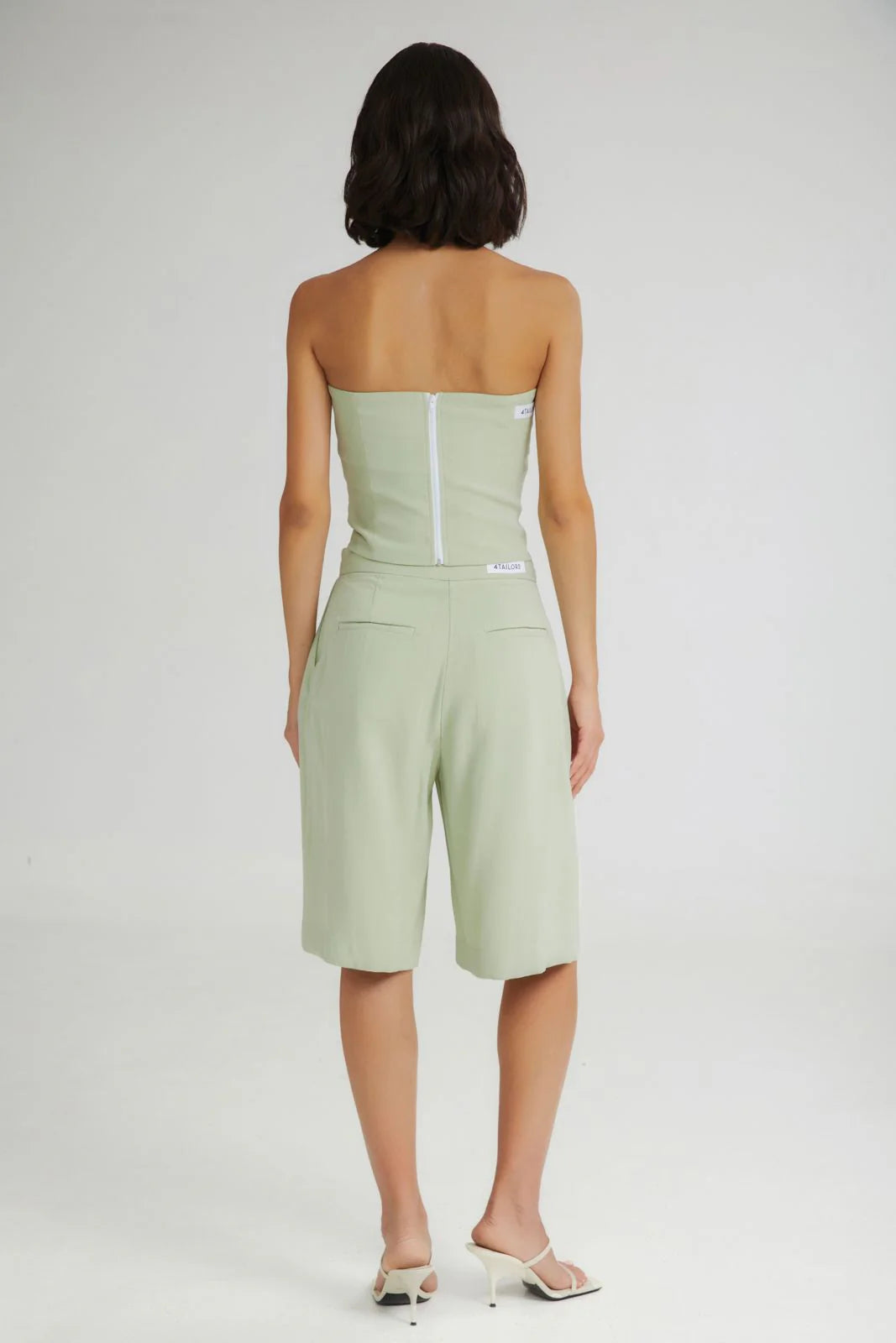 Woman wearing a light green strapless top and shorts on a white background