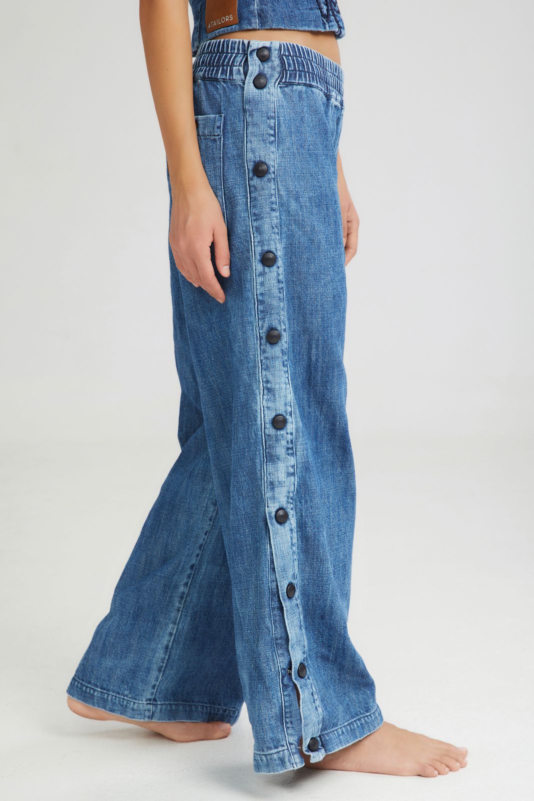 Blue denim wide-leg pants with button details on a white background