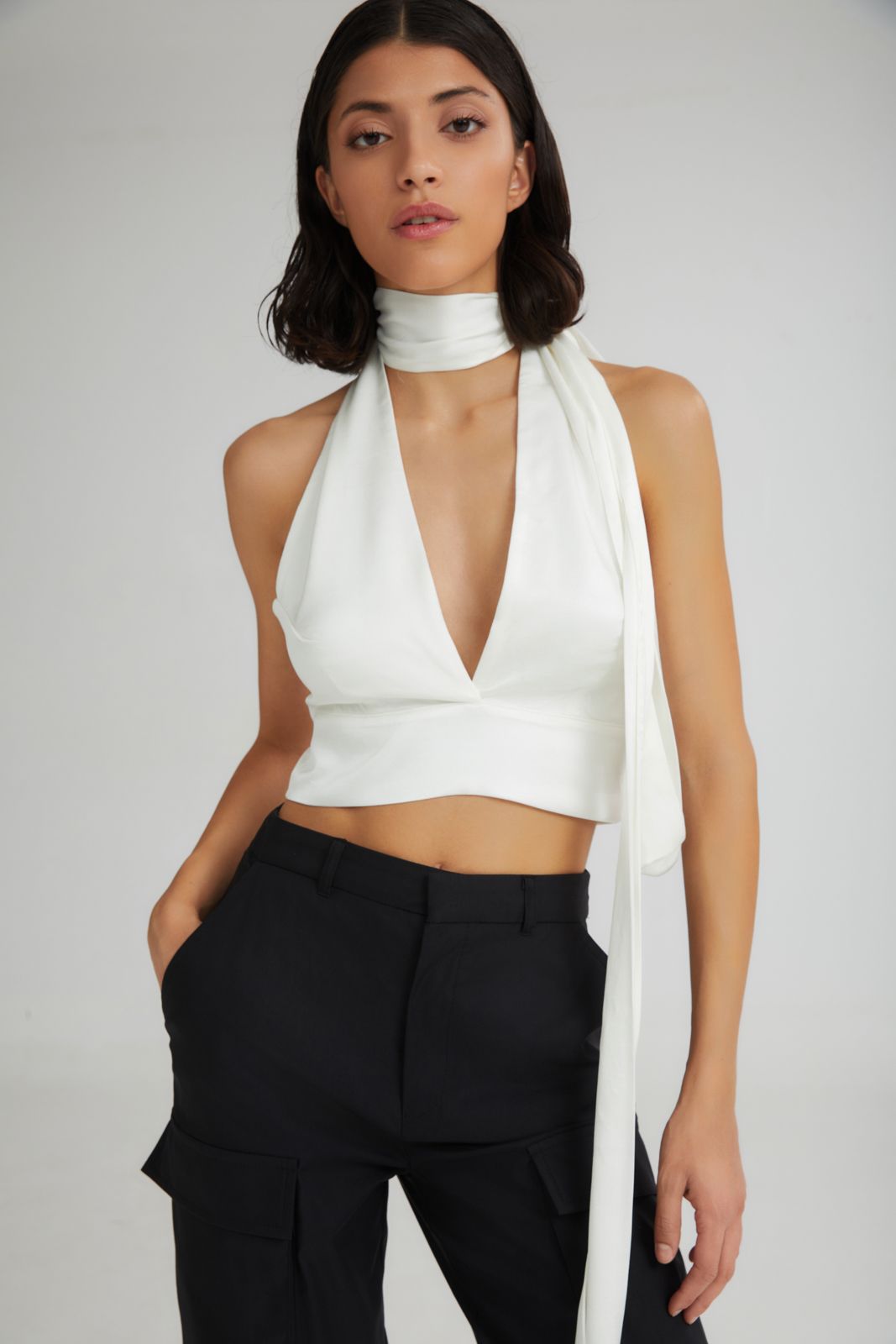 Woman wearing a white halter top and black pants on a plain background