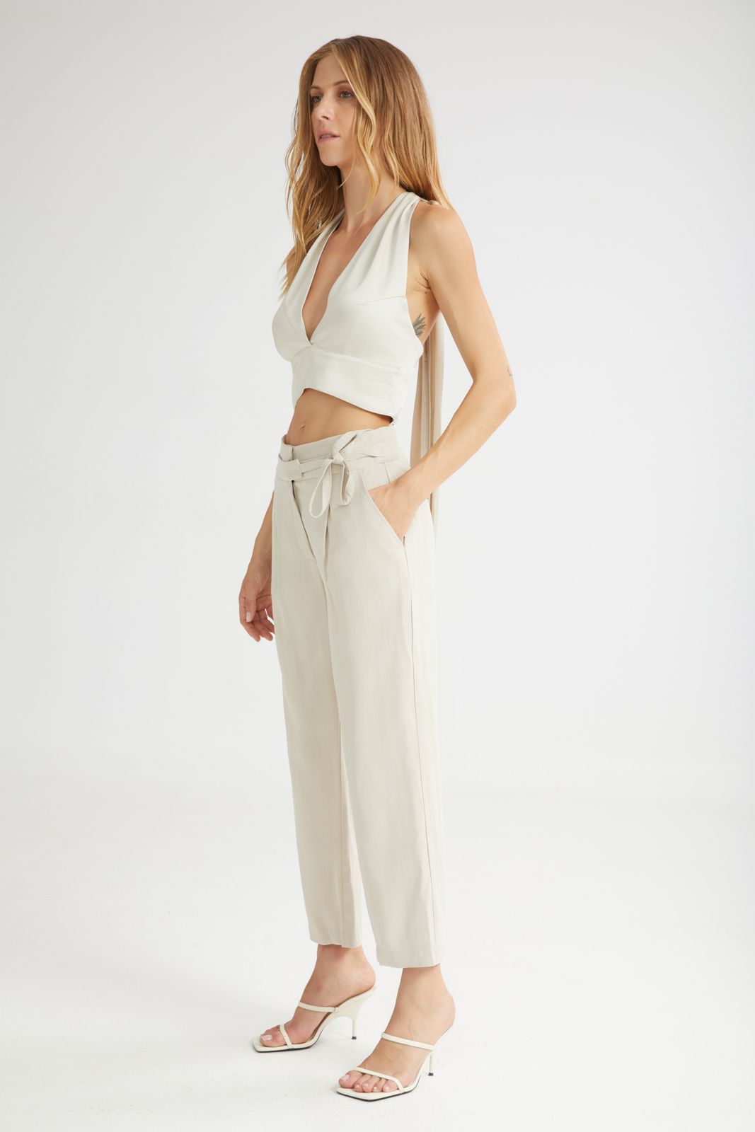 Woman wearing a white sleeveless top and beige pants on a white background