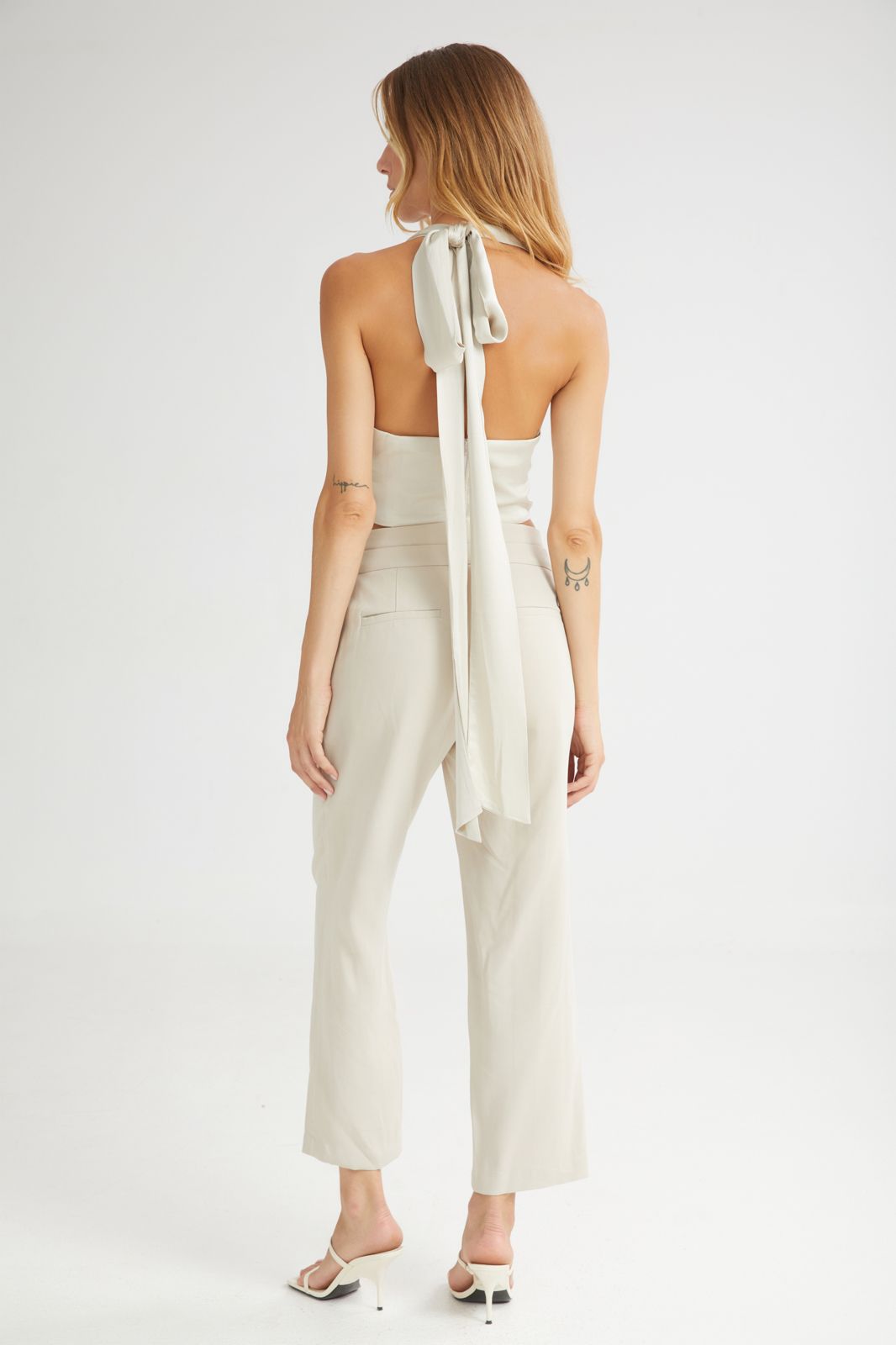 Woman wearing a white strapless top with a bow detail and matching pants on a white background