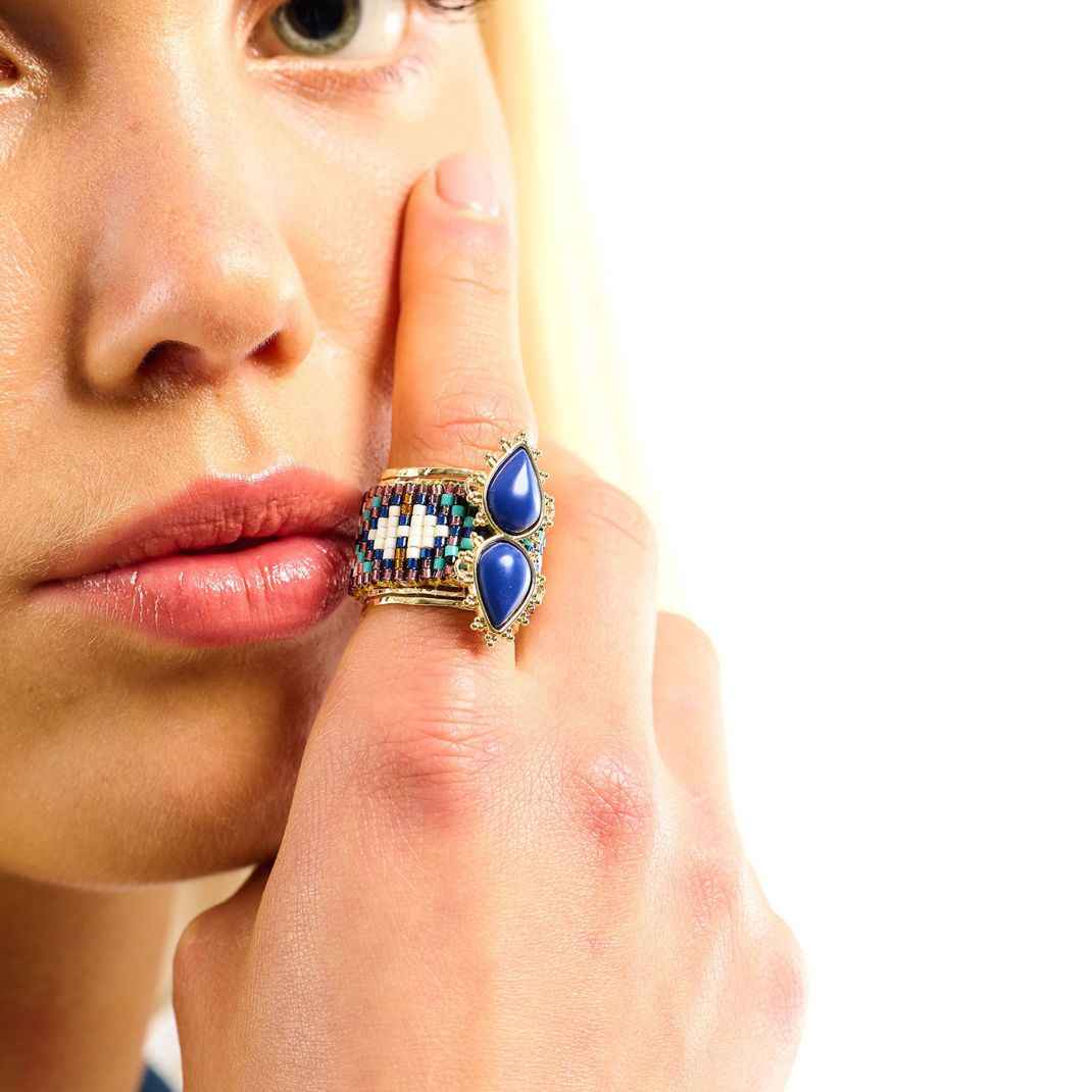Close-up of a woman's hand wearing a decorative ring with blue stones on a white background