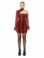 A model wearing a red and black snakeskin-patterned one-shoulder mini dress with sheer long sleeves, paired with black tights and black ankle boots, against a solid white background.
