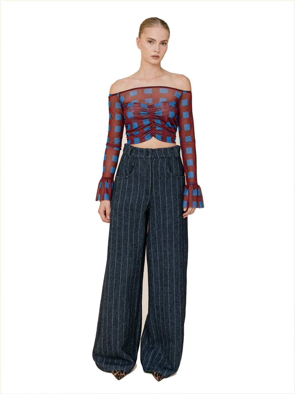 A model wearing a sheer off-the-shoulder long-sleeve crop top with a red and blue checkered pattern, paired with dark blue pinstripe wide-leg trousers, against a plain white background.