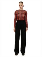 A model stands against a white background wearing a sheer, textured red long-sleeve top with black high-waisted wide-leg trousers.