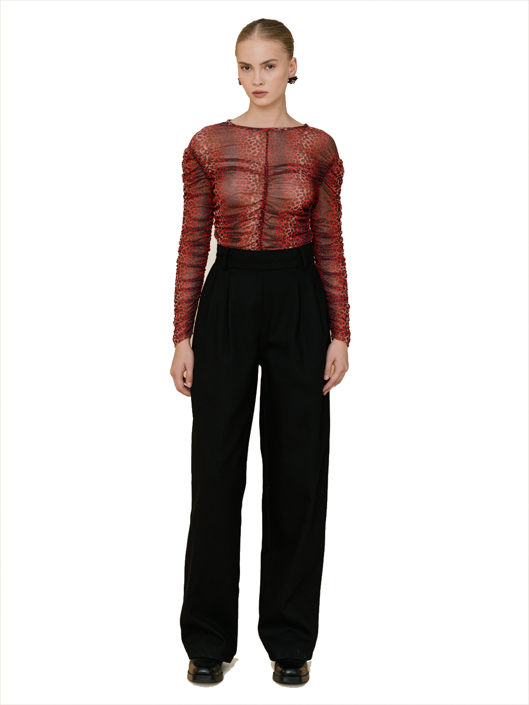 A model stands against a white background wearing a sheer, textured red long-sleeve top with black high-waisted wide-leg trousers.
