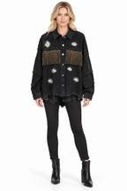 A woman modeling a black distressed denim jacket with fringe and embroidered details, paired with black skinny jeans and black ankle boots, against a plain white background.