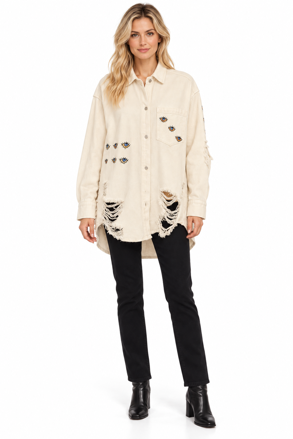 A woman modeling a distressed off-white button-up shirt jacket with ripped details and decorative patches, paired with black pants and black ankle boots, on a white studio background.