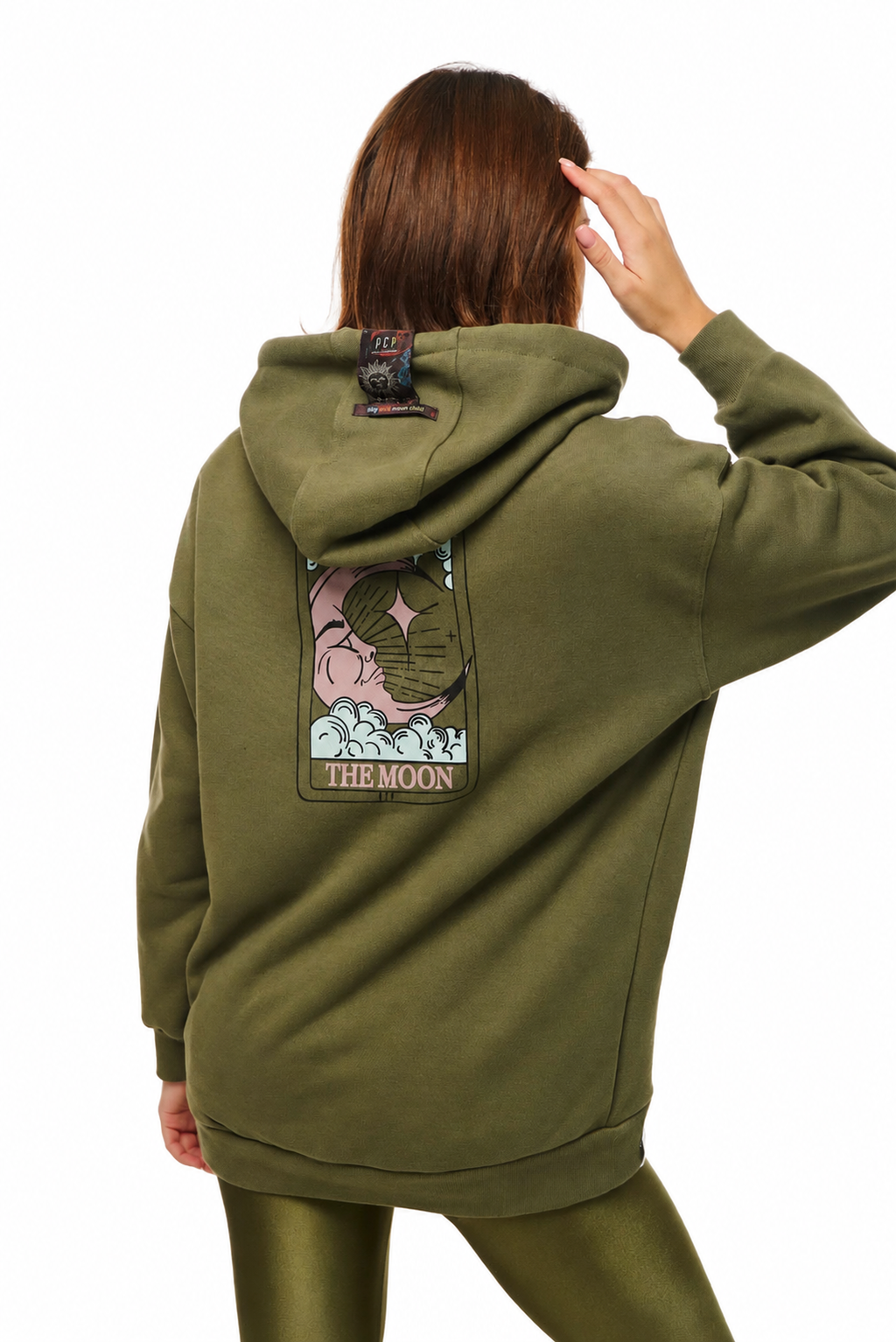 A model shown from the back wearing an olive green hoodie with a large graphic patch on the back that reads 'THE MOON' and features a pink moon illustration, paired with matching olive green leggings against a white background.