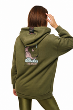 A model shown from the back wearing an olive green hoodie with a large graphic patch on the back that reads 'THE MOON' and features a pink moon illustration, paired with matching olive green leggings against a white background.