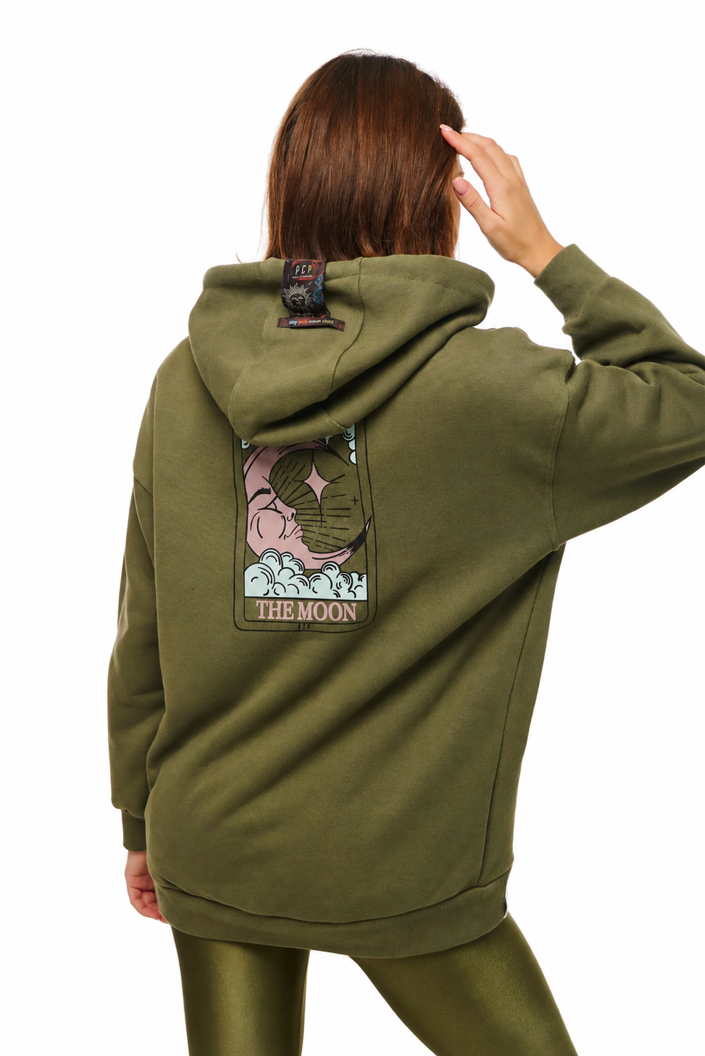 A model shown from the back wearing an olive green hoodie with a large graphic patch on the back that reads 'THE MOON' and features a pink moon illustration, paired with matching olive green leggings against a white background.