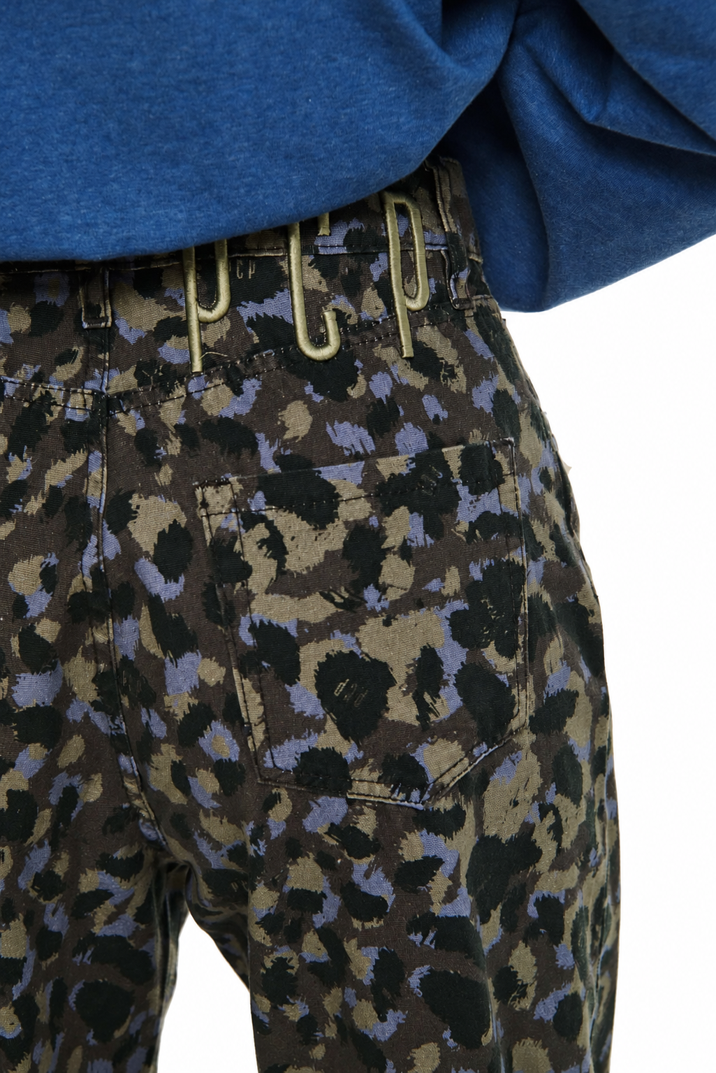 Close-up of a person wearing patterned pants with a blue top, showing the back pocket and waist area against a white background.