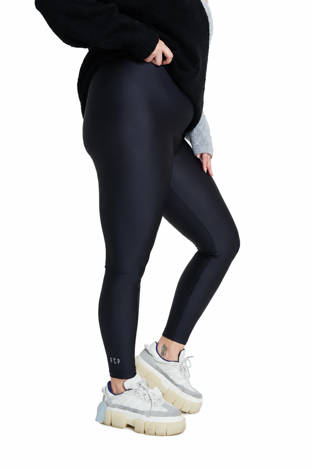 A model wearing black full-length leggings, a black fuzzy sweater, and chunky white platform sneakers, shown from the waist down against a solid white background.