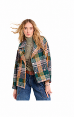 A woman modeling a multicolor plaid blazer over an olive green turtleneck and blue jeans, set against a plain white background.