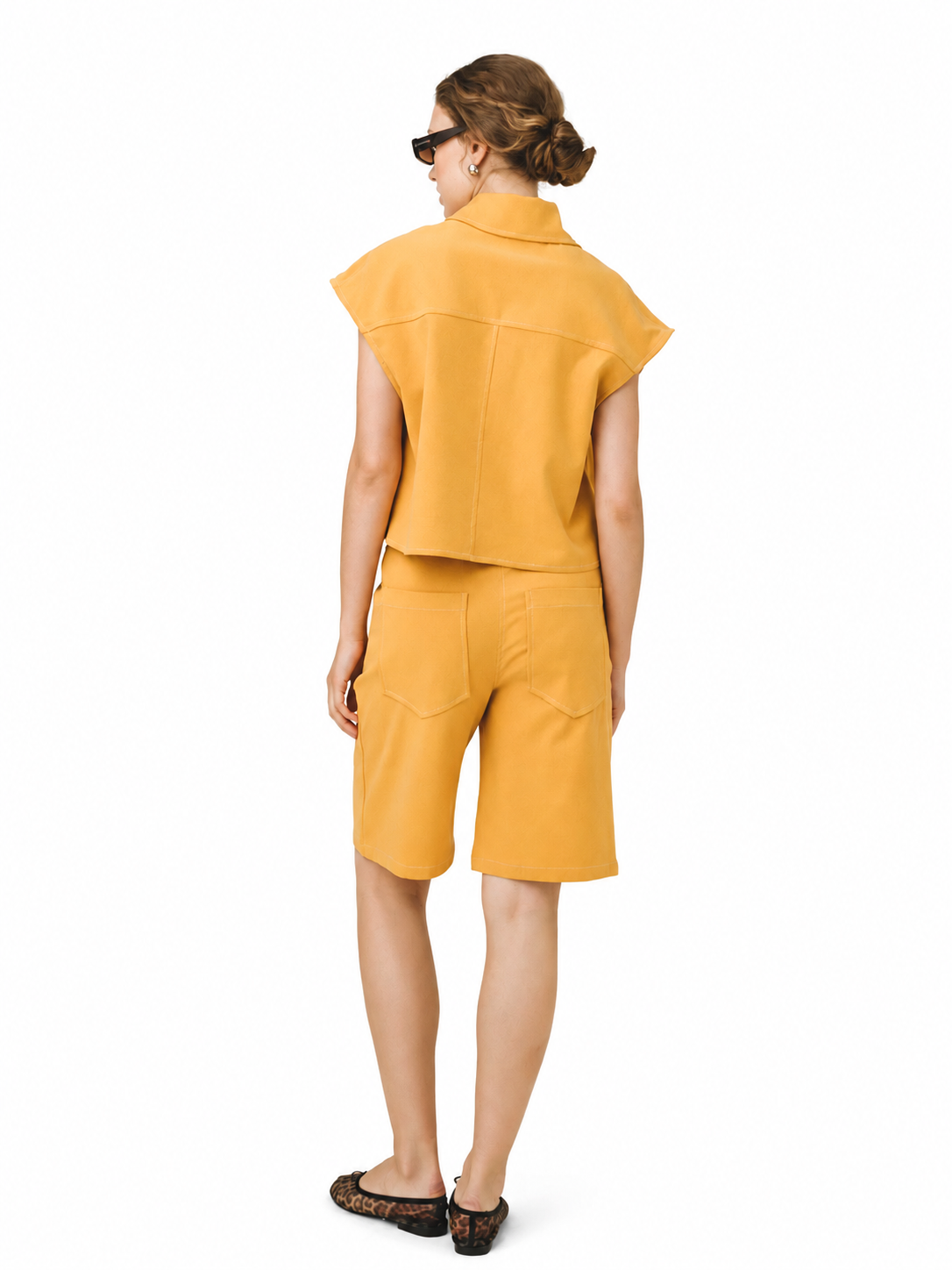 A woman shown from the back wearing a matching mustard yellow two-piece outfit consisting of a short-sleeve cropped shirt and shorts, paired with leopard-print flats, on a white background.