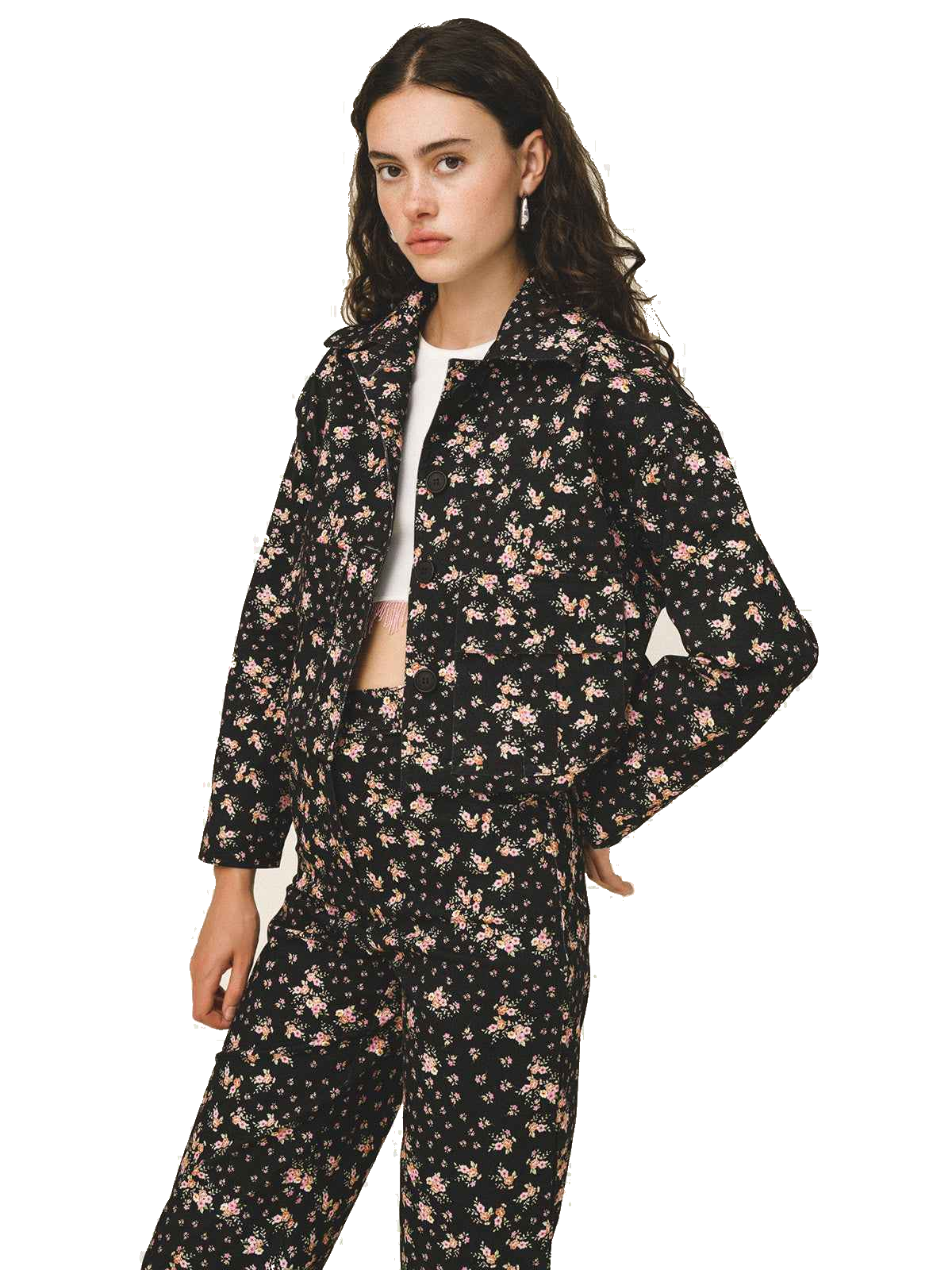 A woman modeling a matching two-piece floral print set consisting of a long-sleeve collared jacket and coordinating pants, featuring a black base with pink and beige floral motifs.