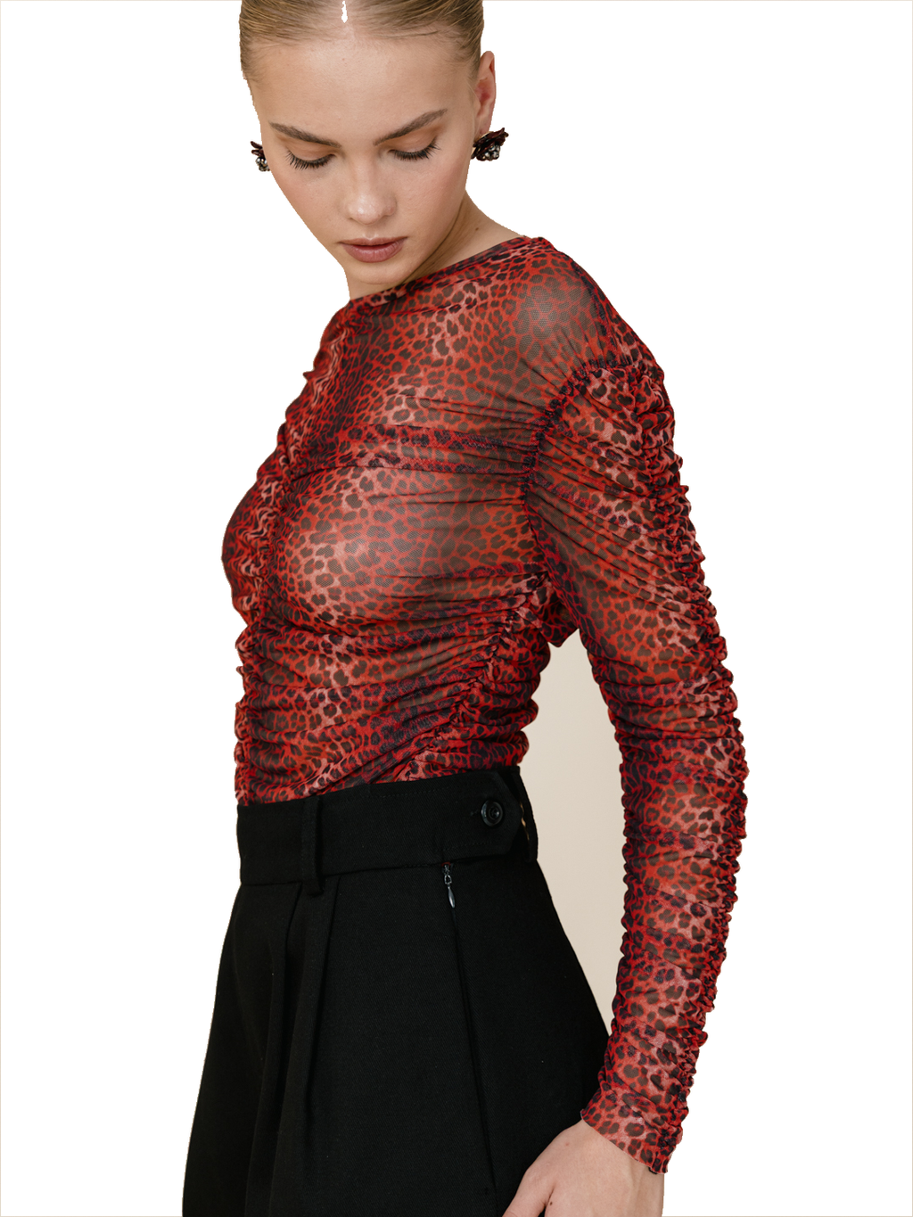 A model wearing a sheer, long-sleeve top with a red and black leopard print pattern, paired with black trousers, against a plain white background.