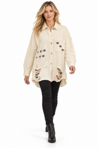 A woman modeling a distressed off-white button-up shirt jacket with embroidered details, paired with black skinny jeans and black ankle boots, on a solid white background.